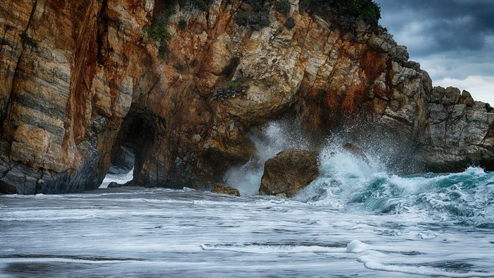 Waves crashing against a rocky cliff face with a cave
