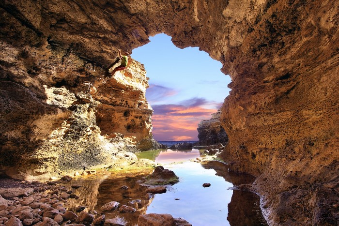 Rock climber in a sea cave at sunset