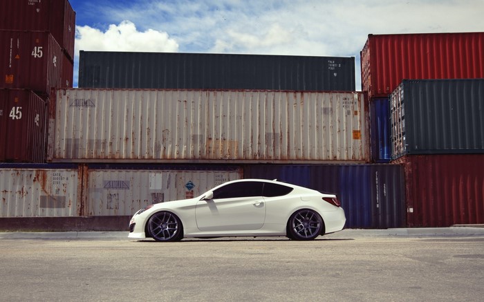 White Hyundai Genesis Coupe parked by shipping containers