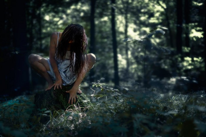 Woman in a white dress crouching in a dark forest