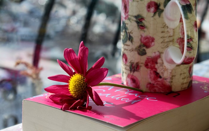Pink flower on a book next to a floral mug