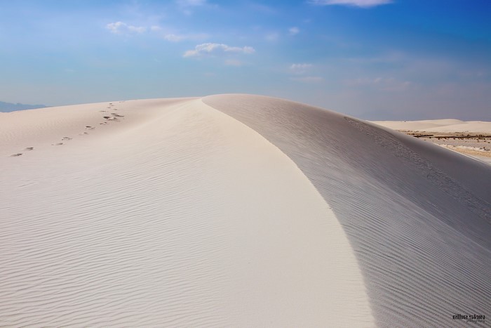 Footprints on a sand dune under a blue sky