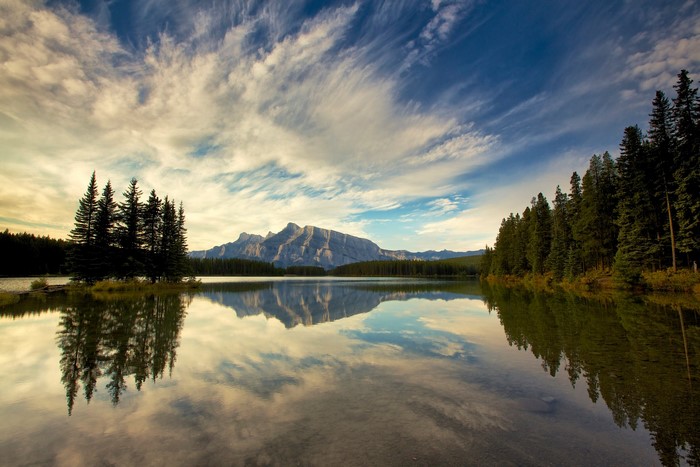 Mountain reflected in a calm lake with pine trees and clouds