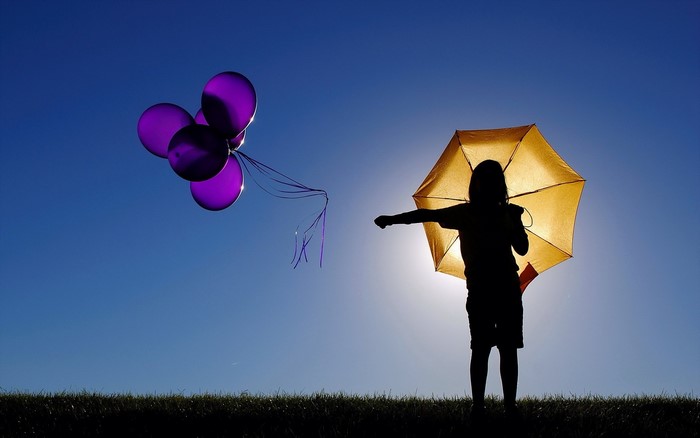 Silhouette of a child holding an umbrella with balloons