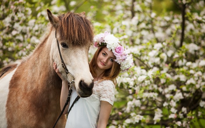 Girl with flower crown and horse in spring orchard