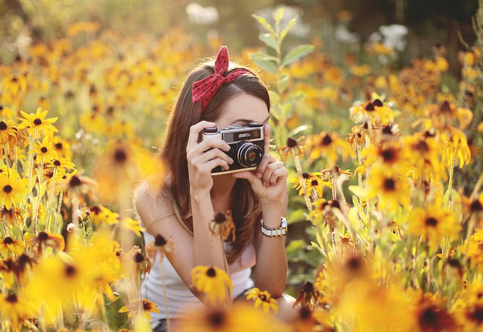 Girl with camera in a field of yellow flowers
