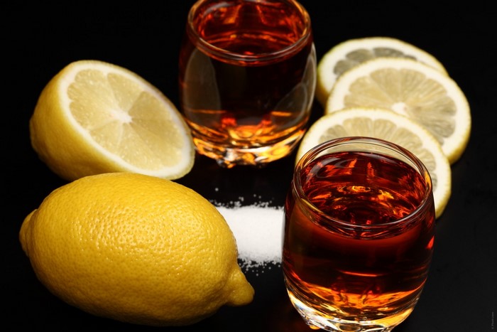 Two shot glasses of amber liquid with lemons and salt