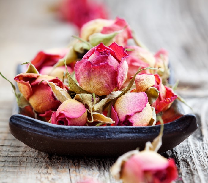 Dried rose buds in a dark bowl on wood