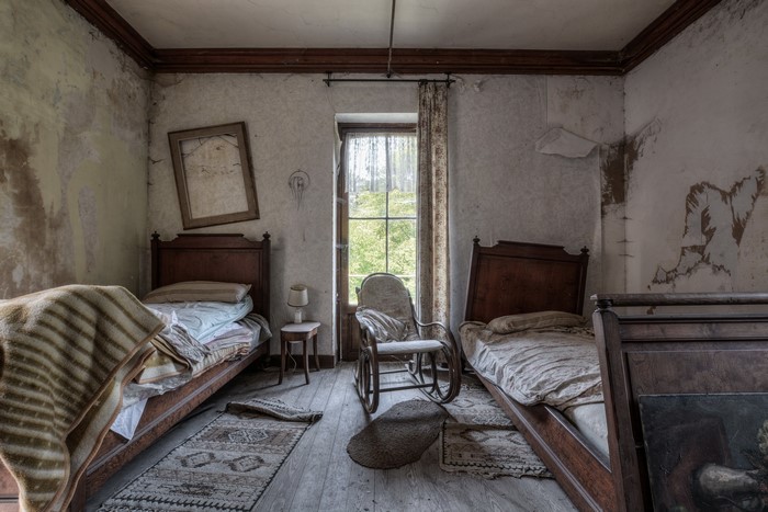 Abandoned bedroom with two beds and a rocking chair