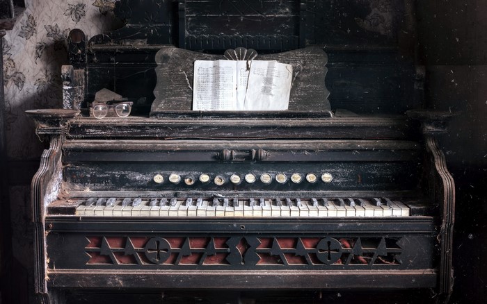 Old dusty piano with sheet music and glasses