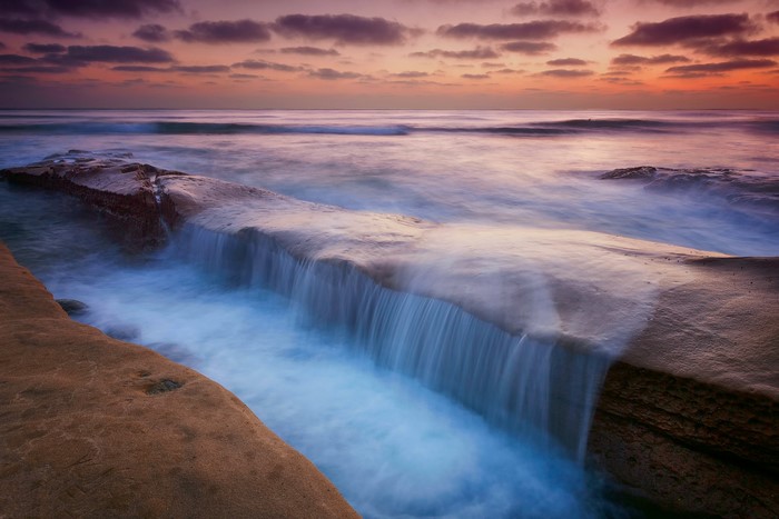 Ocean waves cascading over rocks at sunset