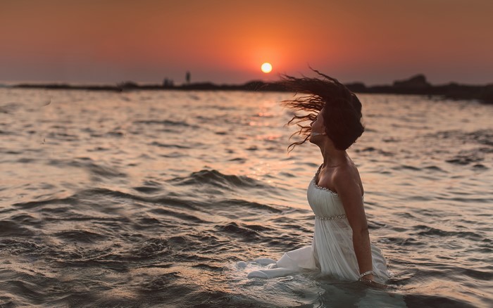 Woman in white dress in the ocean at sunset