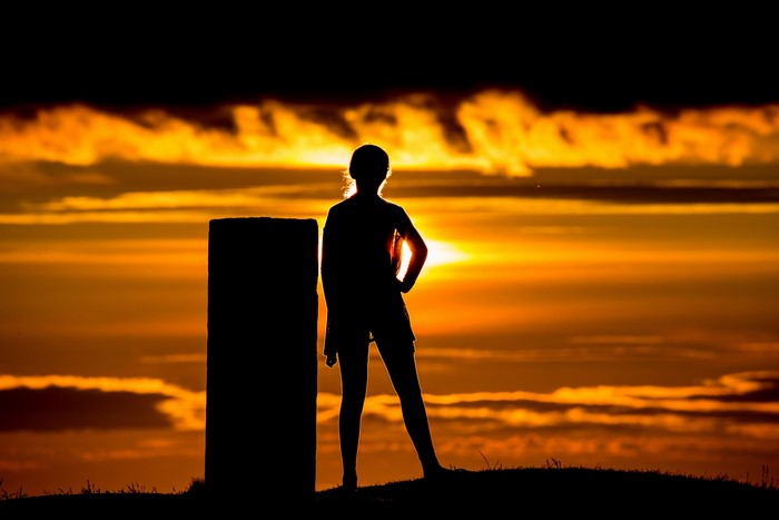 Silhouette of a person standing next to a pillar at sunset