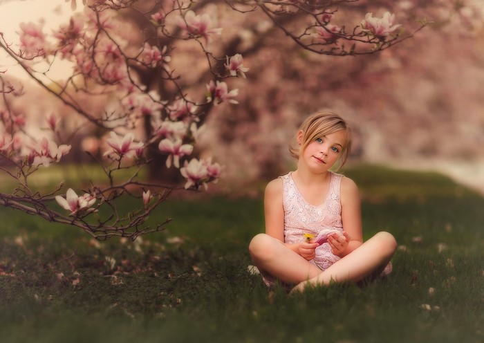 Young girl sitting under a blooming magnolia tree