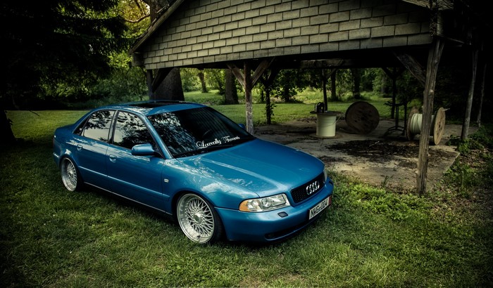 Blue Audi A4 parked on grass near a wooden structure
