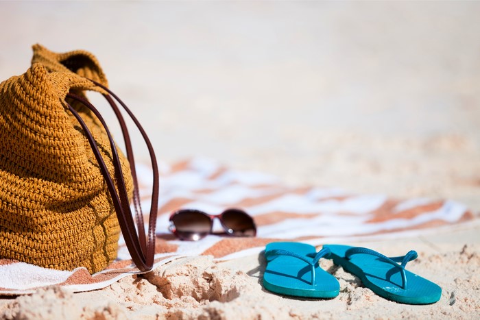 Summer beach accessories: straw bag, sunglasses, flip-flops, and towel