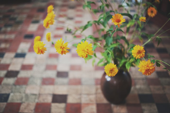 Yellow flowers in a vase on a tiled floor