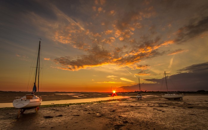 Sailboats on a muddy shore at sunset