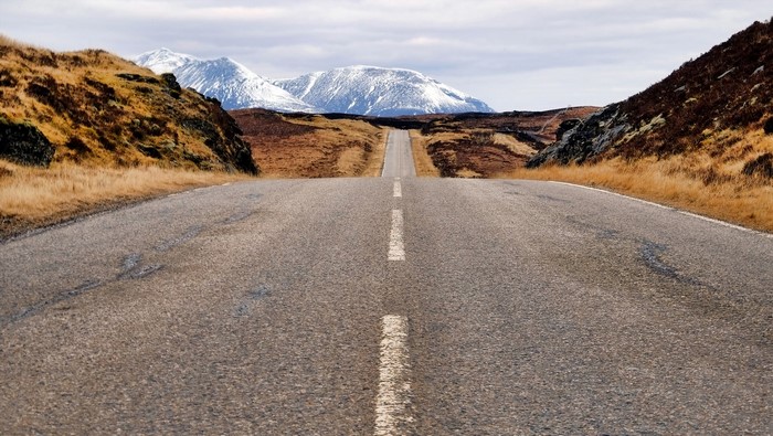 Road through Scottish Highlands with snow-capped mountains