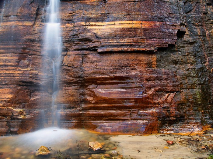 Waterfall cascading down a layered sandstone cliff