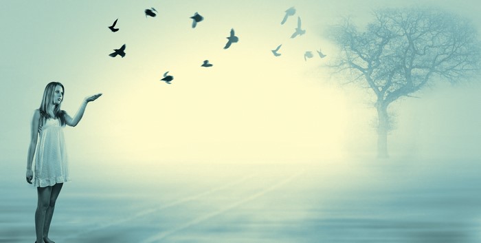 Girl releasing birds in foggy landscape with tree
