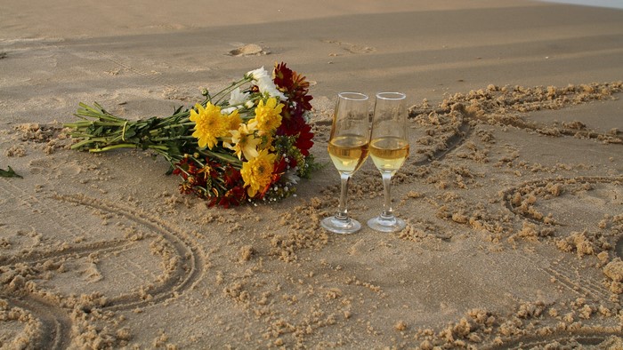 Bouquet and champagne glasses on sand