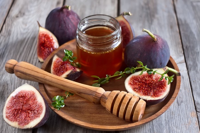 Figs and honey with a honey dipper on a wooden plate