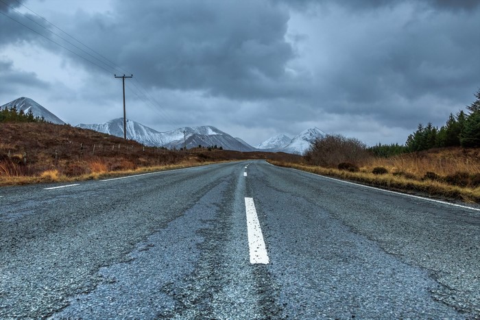 Asphalt road leading to snow-capped mountains under cloudy sky