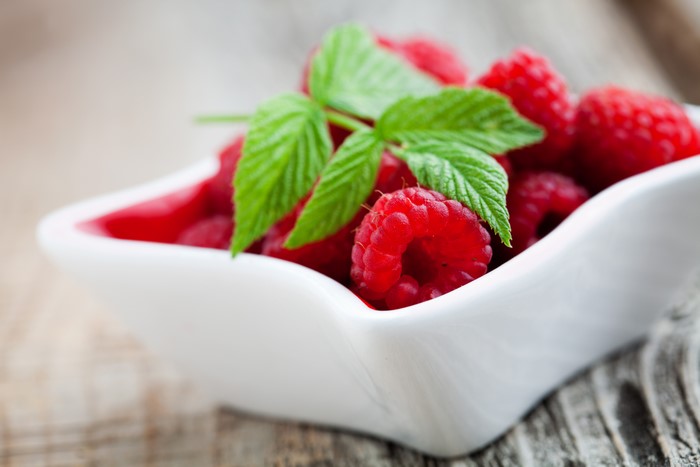 Raspberries in a white bowl with green leaves