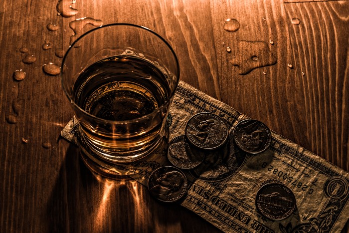 Glass of whiskey with money and coins on a wooden table