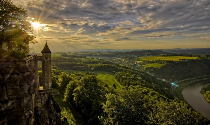 Castle on a cliff overlooking a river valley at sunset