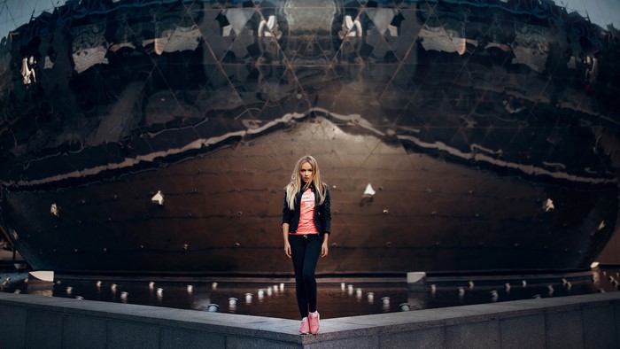 Woman in black jacket and pink top near a large spherical building with fountains