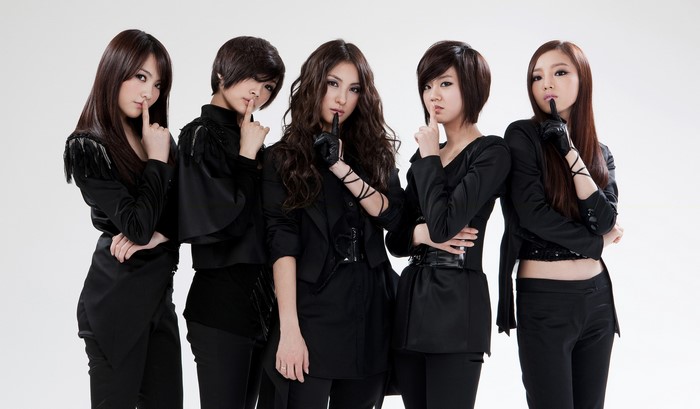 Five women in black outfits posing with fingers to lips