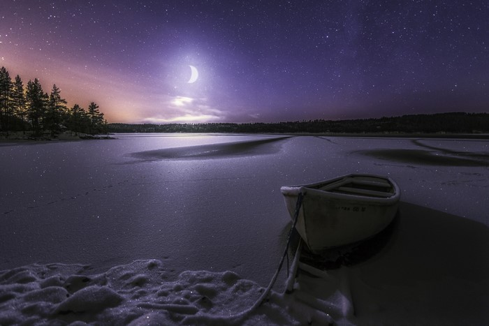Boat on a frozen lake under a starry night sky in Norway