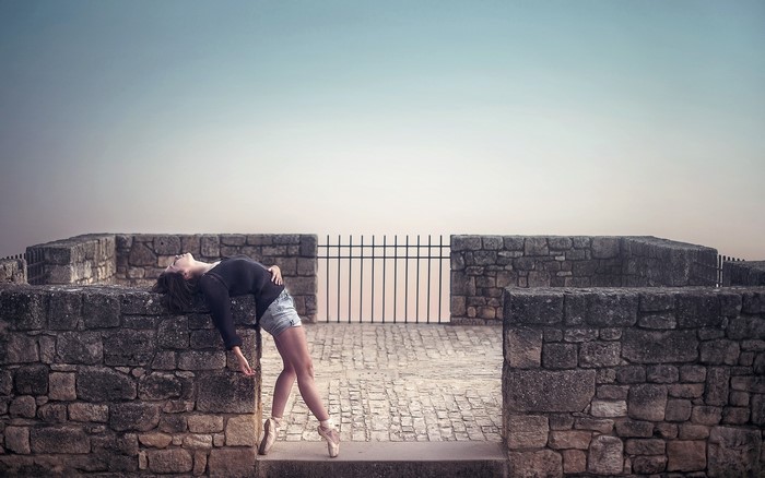 Ballerina leaning on stone wall with fence