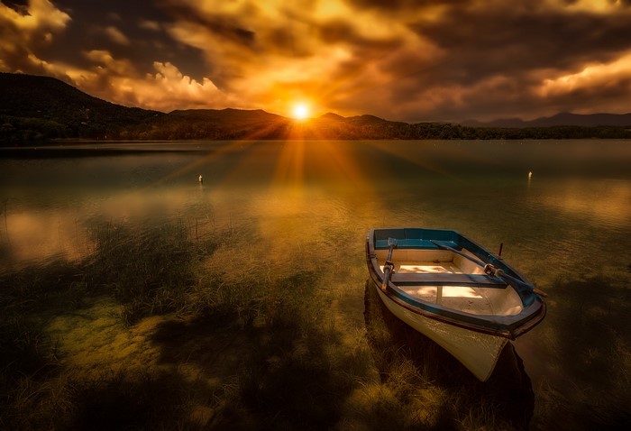 Boat on Lake Banyoles at sunset with sun rays
