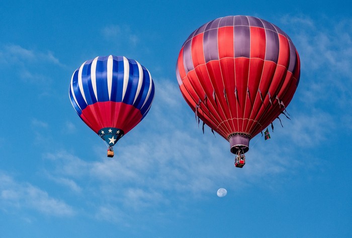 Two hot air balloons in a blue sky with clouds