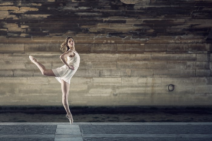 Ballerina in white dress performing ballet under a stone bridge