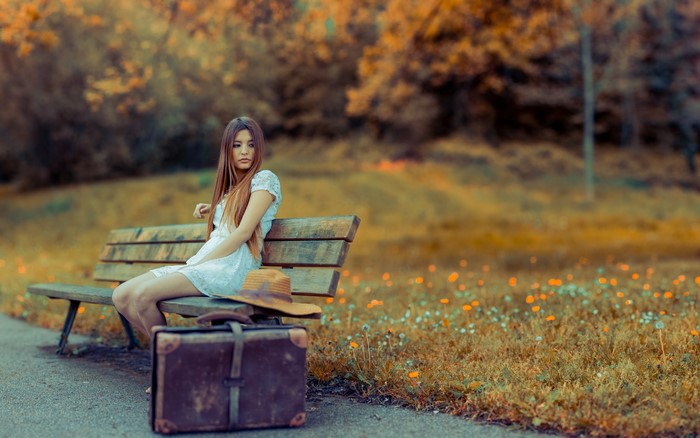 Woman sitting on a park bench with a suitcase