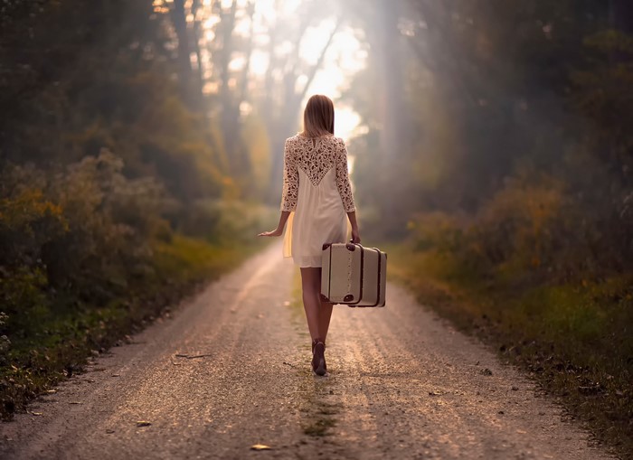 Woman walking on a dirt road with a suitcase