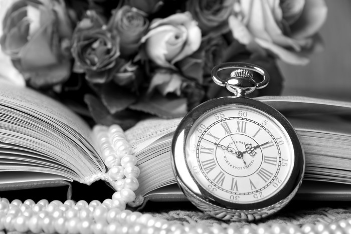Pocket watch on an open book with roses and pearls