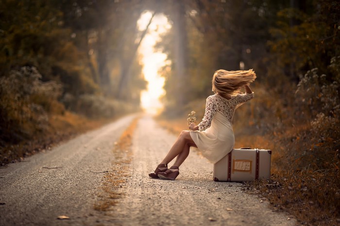 Woman sitting on suitcase on a road
