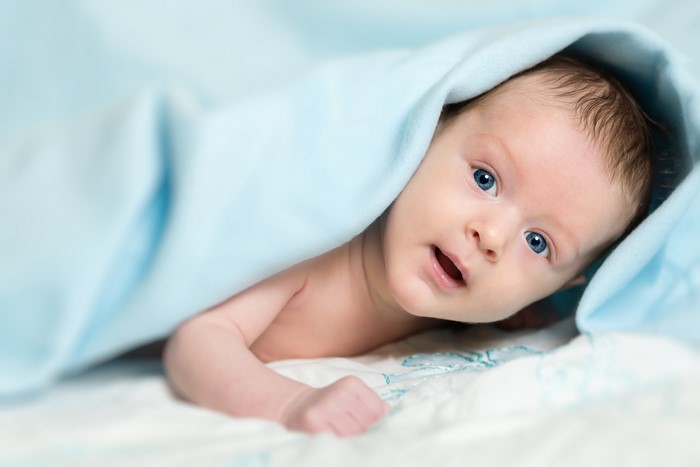 Infant peeking from under a blue blanket