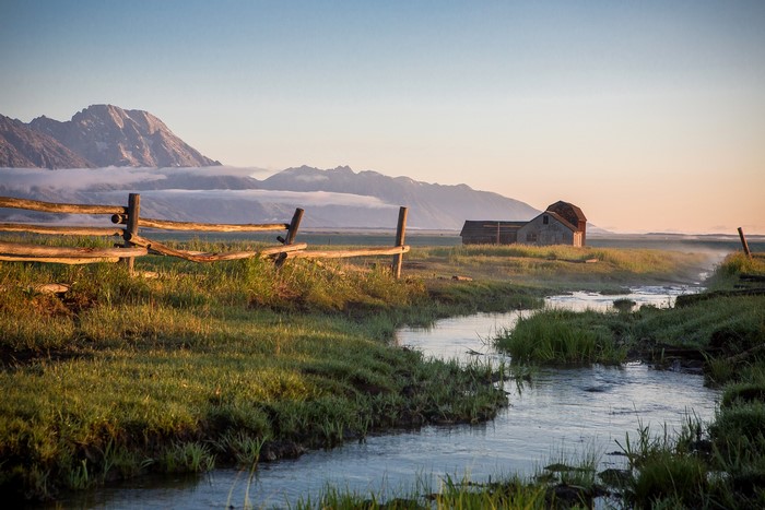 Barn and fence by mountains with fog and stream