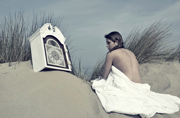 Woman and grandfather clock on a sandy beach