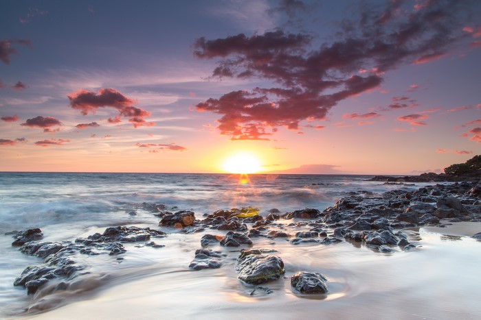 Sunset over the ocean with rocks and clouds in Hawaii
