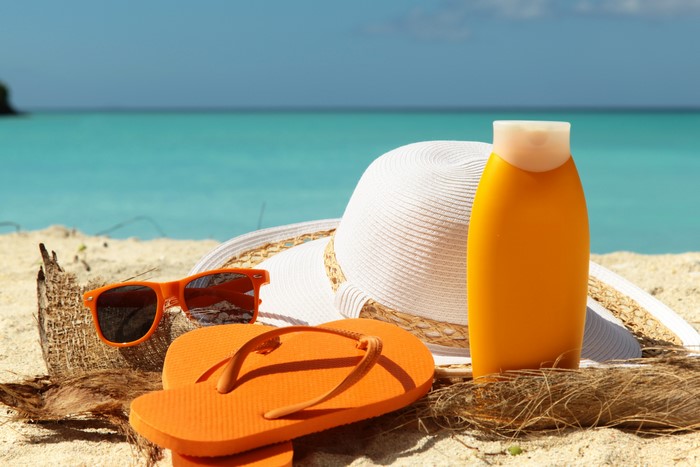 Summer beach accessories: sunglasses, hat, flip-flops, and sunscreen
