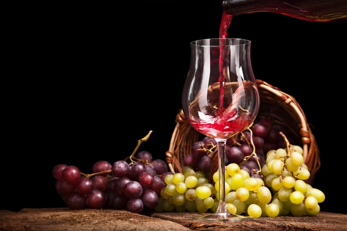 Red wine being poured into a glass with grapes