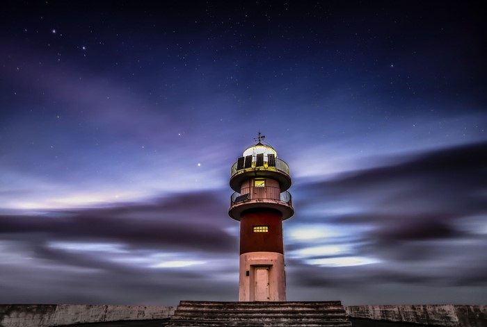 Lighthouse under a starry night sky with clouds