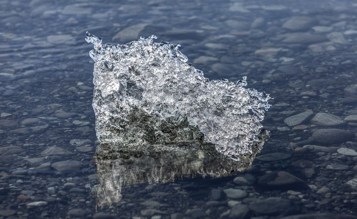 Ice fragment floating in shallow water with pebbles